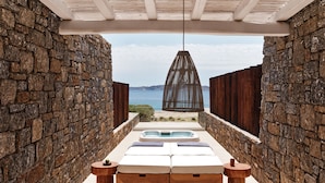 A sunlit outdoor seating area with stone walls, a wooden bench, and a table with a bowl and cup. - Bill&Coo Mykonos (Mykonos)