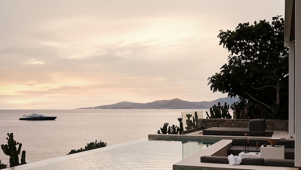 A pool with a view of the sea and mountains, a yacht in the distance, and a cactus garden. - Bill&Coo Mykonos (Mykonos)