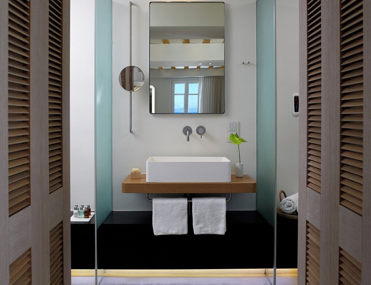 A modern bathroom with a rectangular sink, two towel racks, a mirror, and a plant.