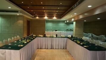 Un salón de conferencias con una larga mesa, sillas blancas y un mantel verde.