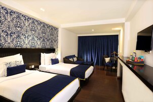 Une chambre d’hôtel avec deux lits, un bureau, un téléviseur  à écran plat et une grande fenêtre avec des rideaux.