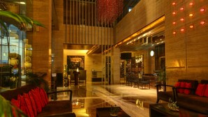 A spacious lobby with a high ceiling, a central seating area with sofas and a coffee table, and a reception desk. - Mosaic Original, Noida (Noida)