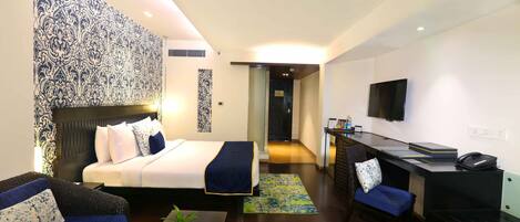 A hotel room with a bed, a desk, a chair, a sofa, and a television.