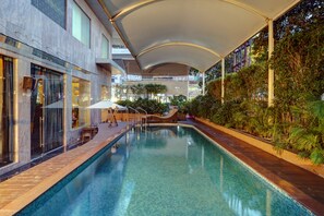 Una piscina interna con soffitto curvo, circondata da piante e un’area relax.
