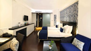 A hotel room with a bed, two sofas, a desk, and a TV. - Mosaic Original, Noida (Noida)