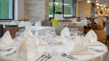A restaurant with round tables set for dining, featuring white tablecloths, silverware, and clear glassware.