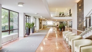Een ruime hotel lobby met een lange receptiebalie, zithoek en een trap naar een hoger niveau.