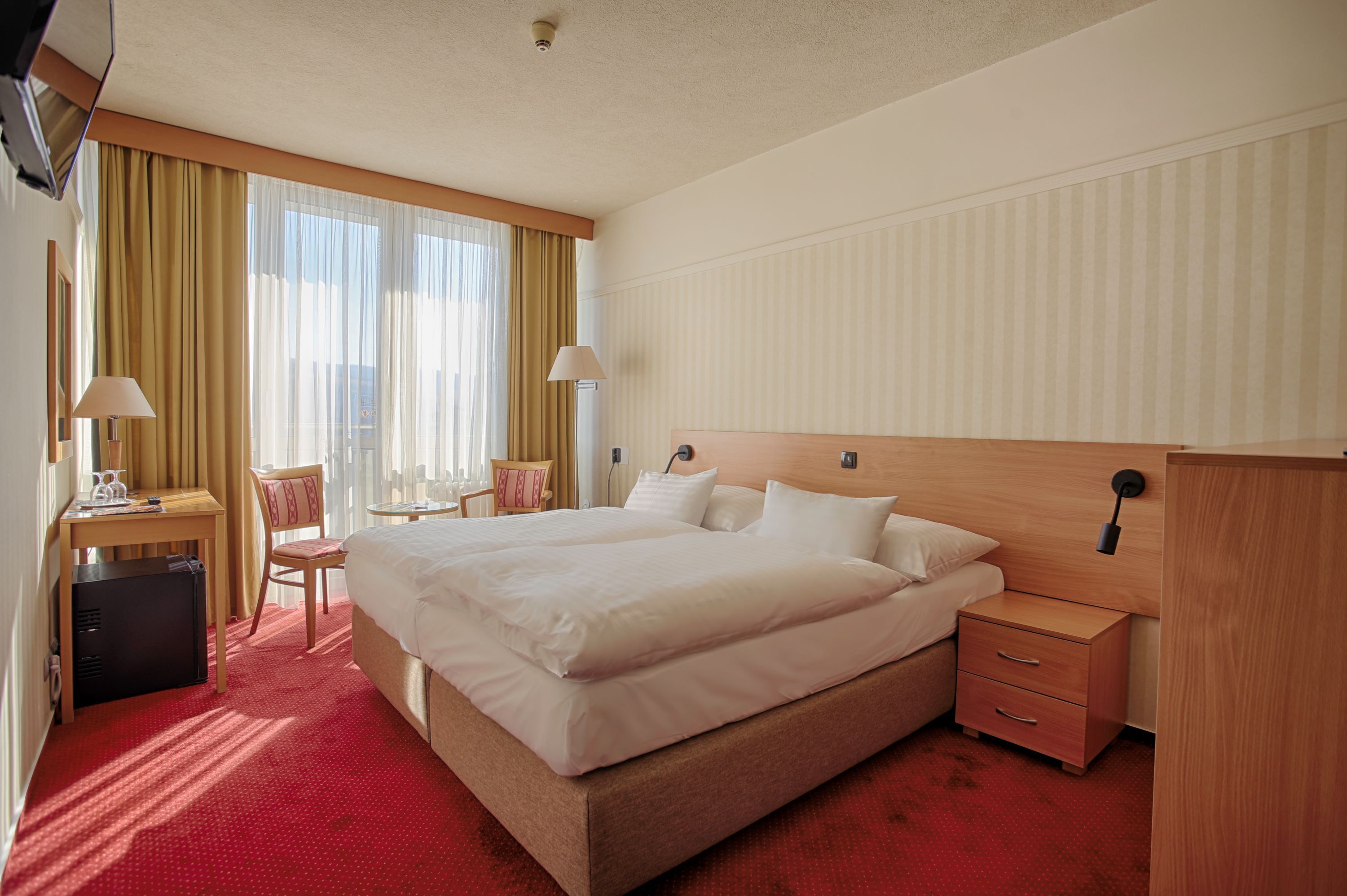 Ein Hotelzimmer mit einem großen Bett, einem Schreibtisch mit Lampe, einem Stuhl, einem kleinen Tisch und einem Kleiderschrank.