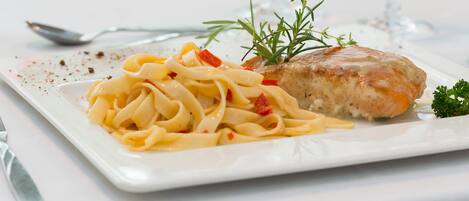 Un plato de pasta con pollo y una ramita de romero.