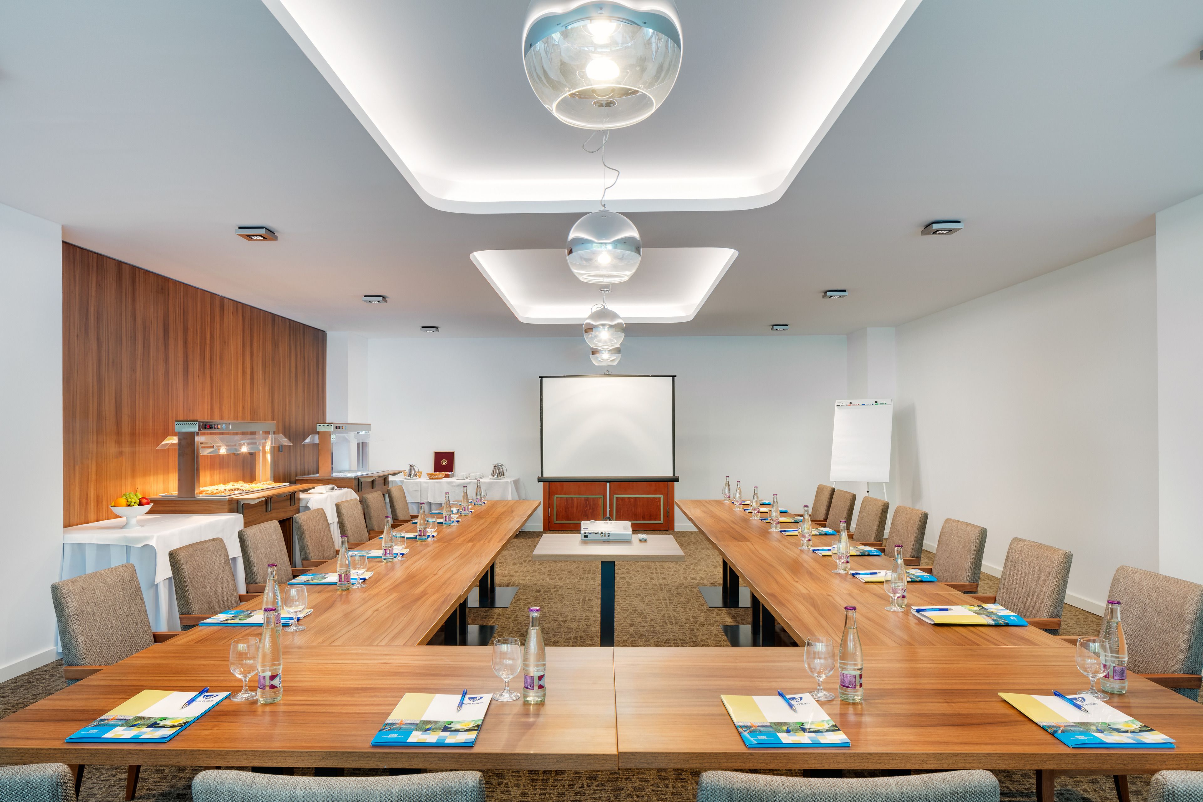 Una sala de conferencias con una larga mesa, sillas, una pantalla de proyector y una pizarra.