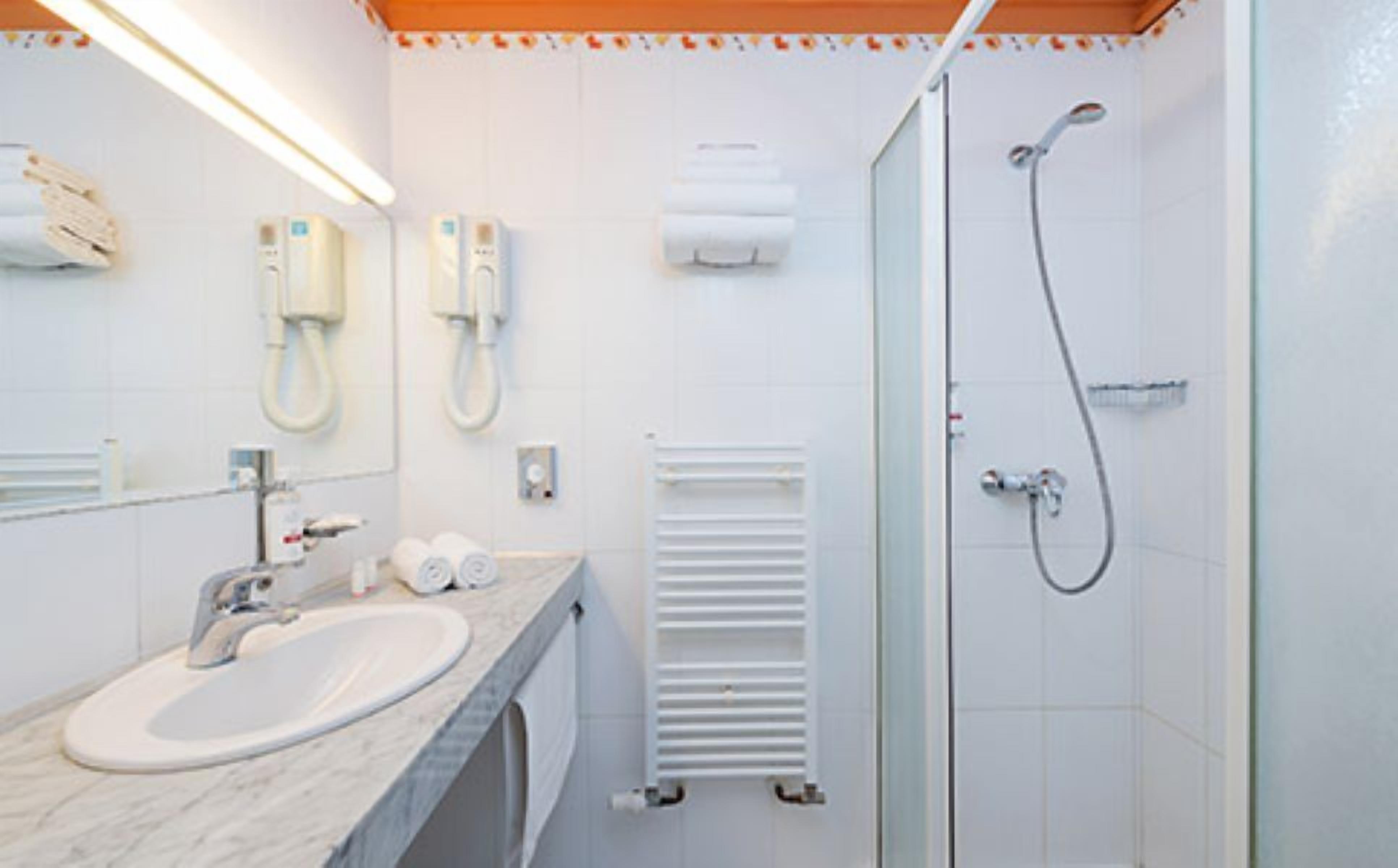 Une salle de bain équipée d’un lavabo, d’un miroir, d’un porte-serviettes et d’un espace douche.