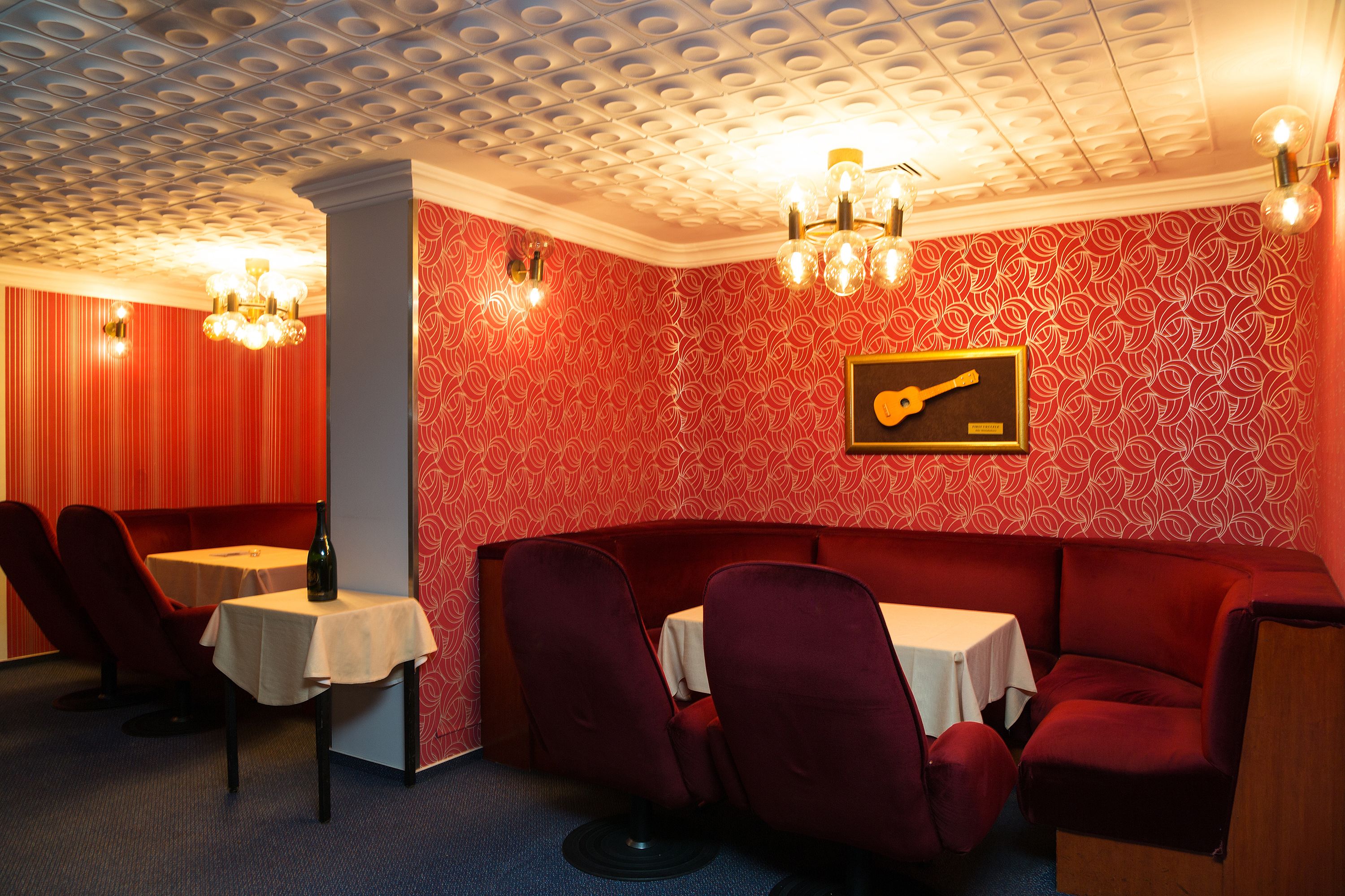 Une pièce avec un mur orné d’un motif rouge, un tableau sur le thème de la guitare, et un canapé rouge accompagné d’une table et de chaises.