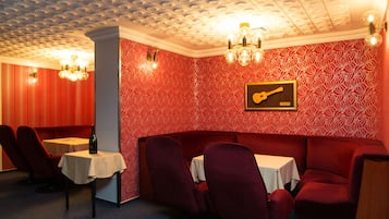 A room with a red patterned wall, a guitar-themed picture, and a red couch with a table and chairs.