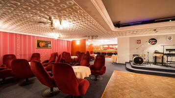 Una sala con sillas y mesas rojas, un escenario con instrumentos musicales y un techo con diseño.