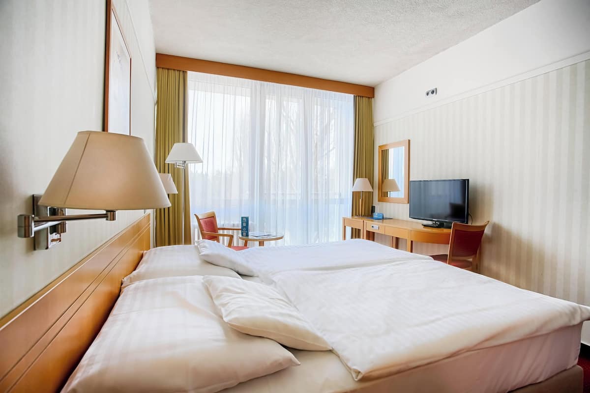 Une chambre d’hôtel avec un lit, deux lampes de chevet, une télévision, un bureau et une chaise.