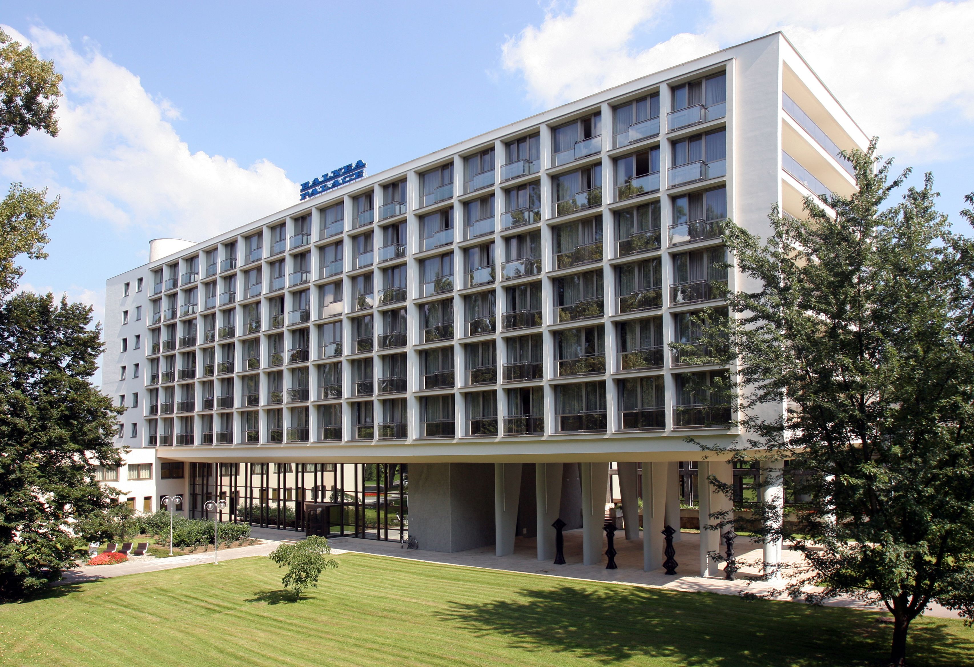 A modern hotel with a grid of balconies, a covered entrance, and a well-maintained lawn.