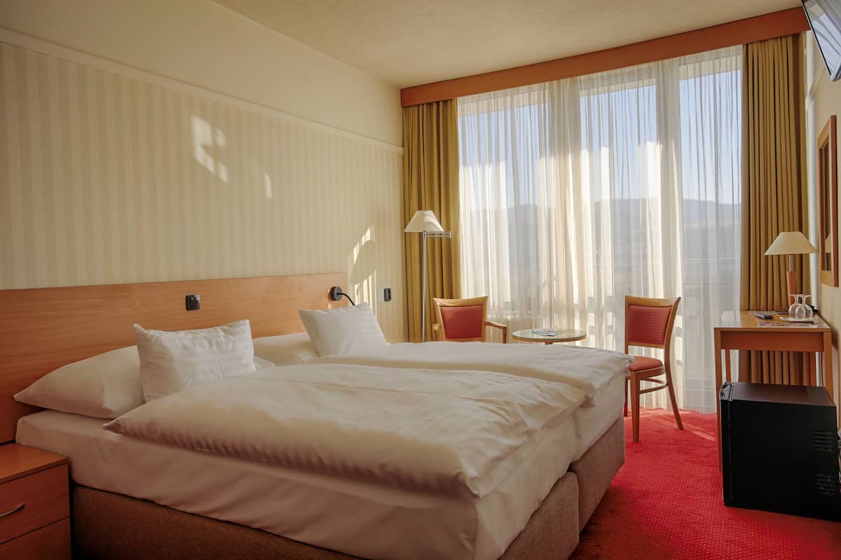 Une chambre d’hôtel avec un grand lit, deux fauteuils, un bureau et une vue sur les montagnes.
