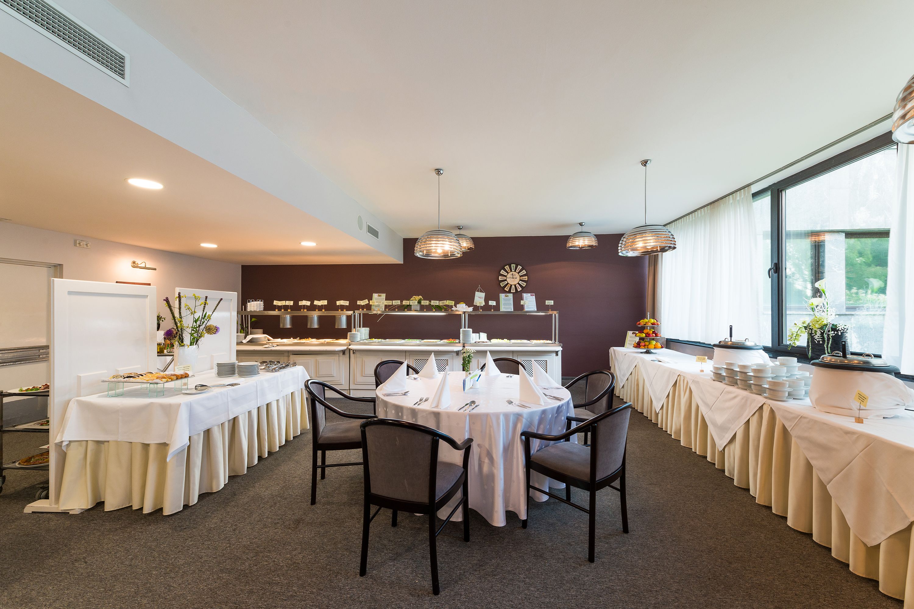 Ein Konferenzraum mit runden Tischen, Stühlen und einem Buffetbereich.