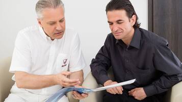 Two men sitting on a couch, one holding a booklet.