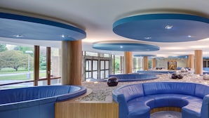 Een moderne lobby met blauwe zitgedeeltes, een fontein in het midden en grote ramen met uitzicht op het omliggende landschap.