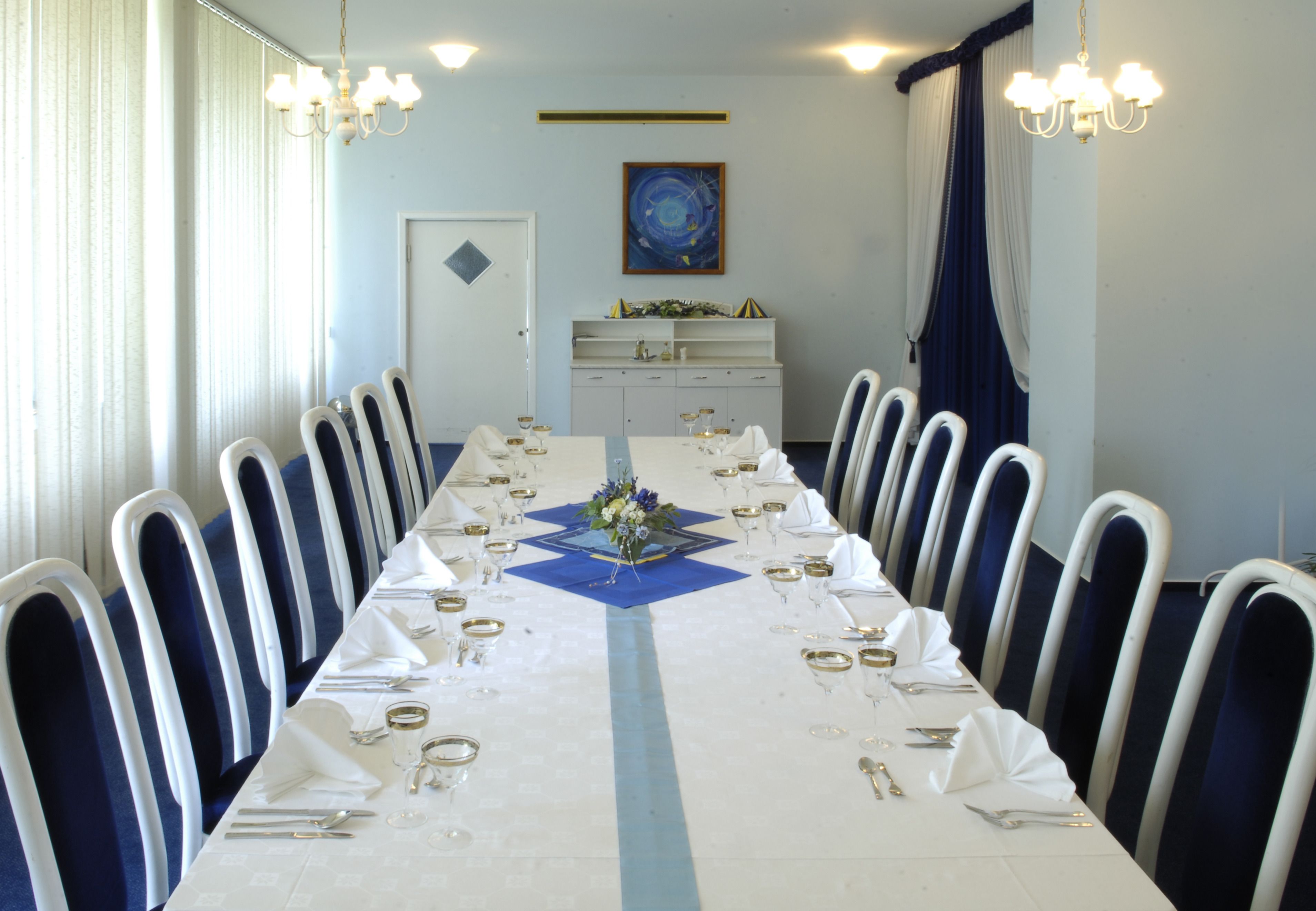 A long dining table set with white tablecloths, blue napkins, and gold cutlery.