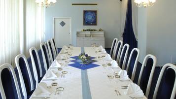 A long dining table set with white tablecloths, blue napkins, and gold cutlery.