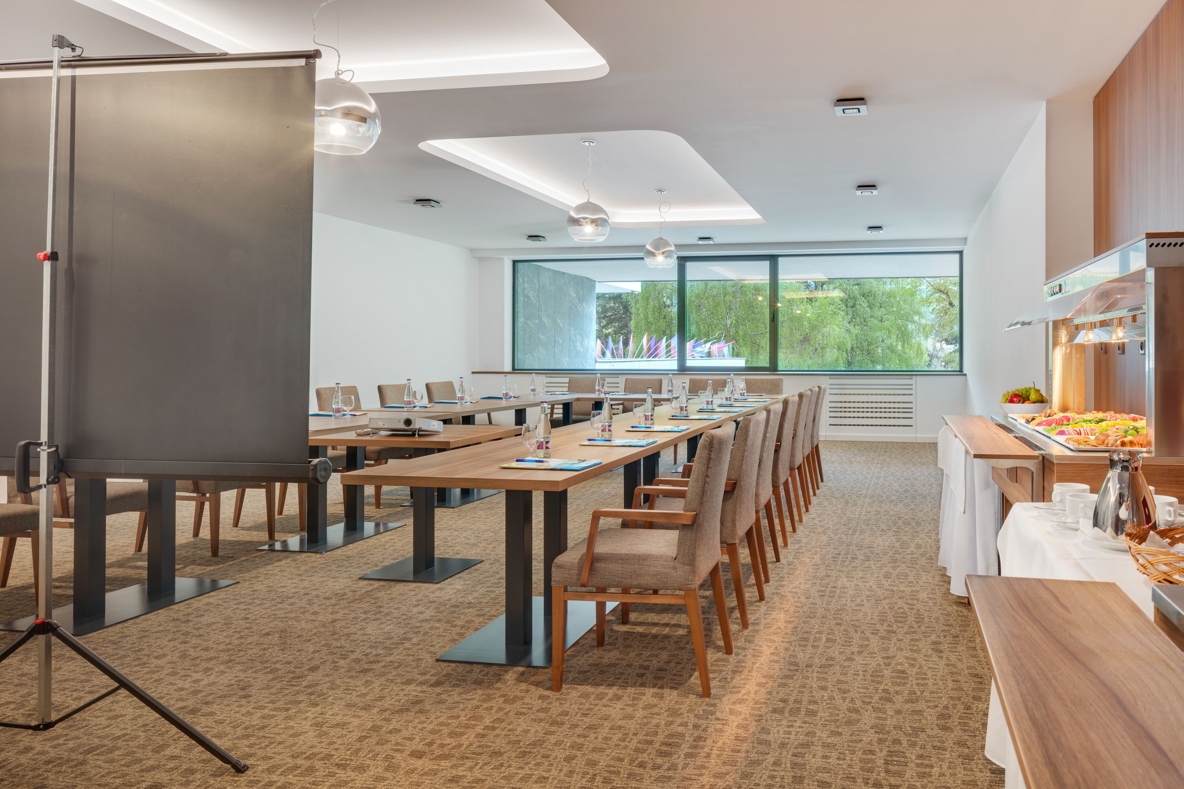 A conference room with long tables, chairs, a projector, and a buffet area.