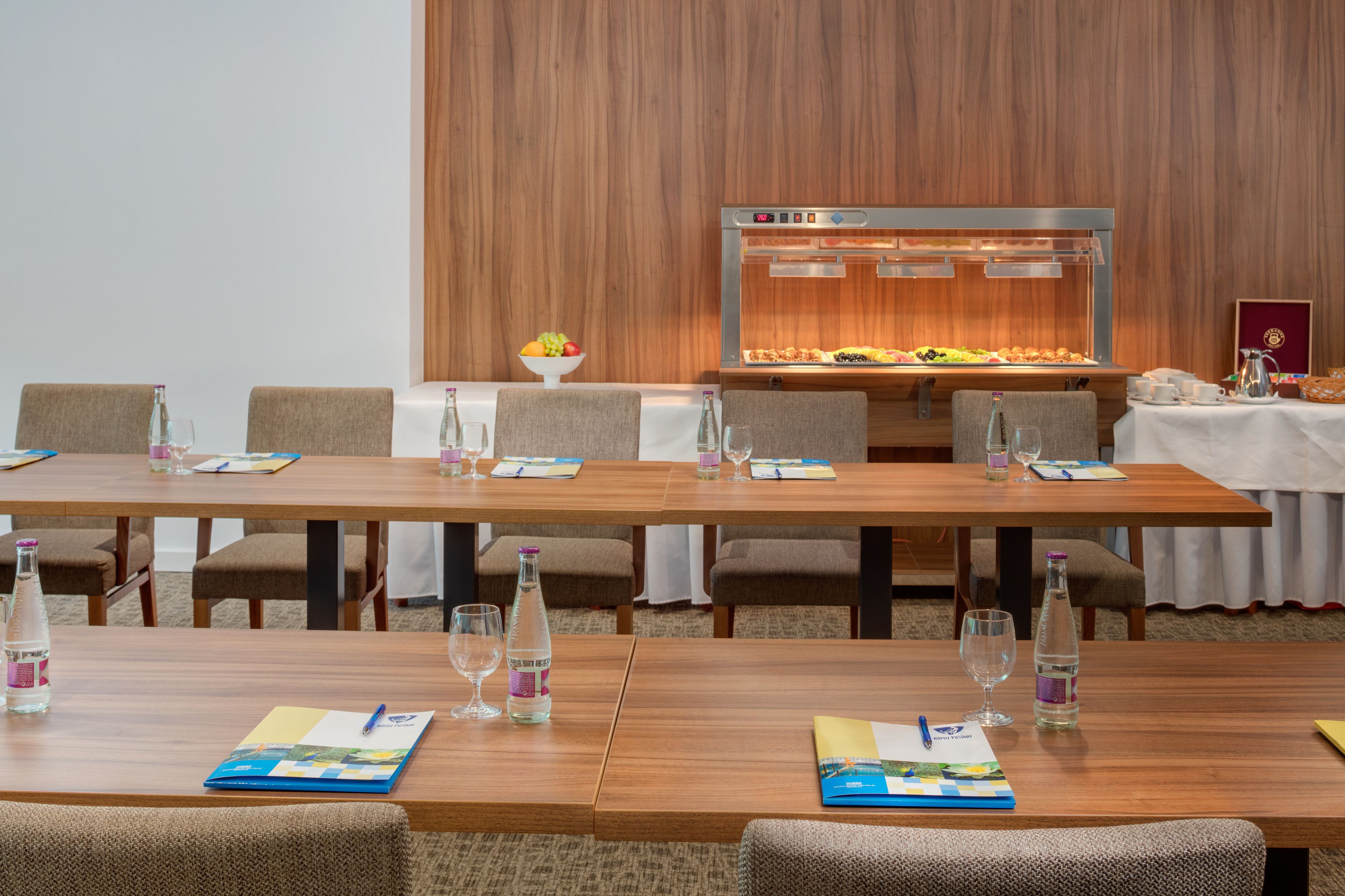 Un salón de conferencias con una larga mesa, sillas, un bufé y una fuente de agua.