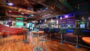 A bar with wooden flooring, metal bar stools, and a counter with bottles.