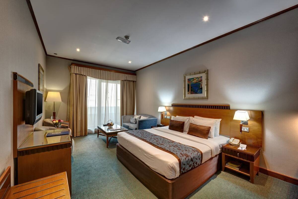 A hotel room with a bed, a desk, a chair, a television, and a window with curtains.