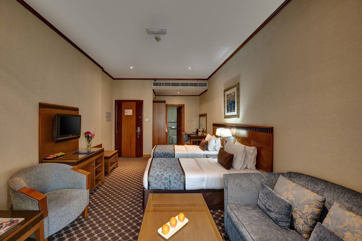 A hotel room with a bed, two sofas, a TV, a desk, and a coffee table.