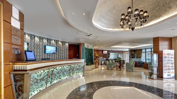A modern hotel lobby with a reception desk, seating area, and a large chandelier.