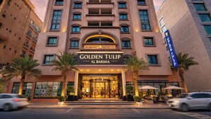 The exterior of the Golden Tulip Al Barsa hotel with a prominent entrance, palm trees, and a clear view of the street.