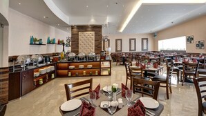A spacious dining area with multiple tables and chairs, a buffet counter with various food items, and a modern ceiling design.
