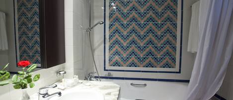 Un baño con un lavamanos blanco, un espejo, ducha y pared de azulejos estampados.