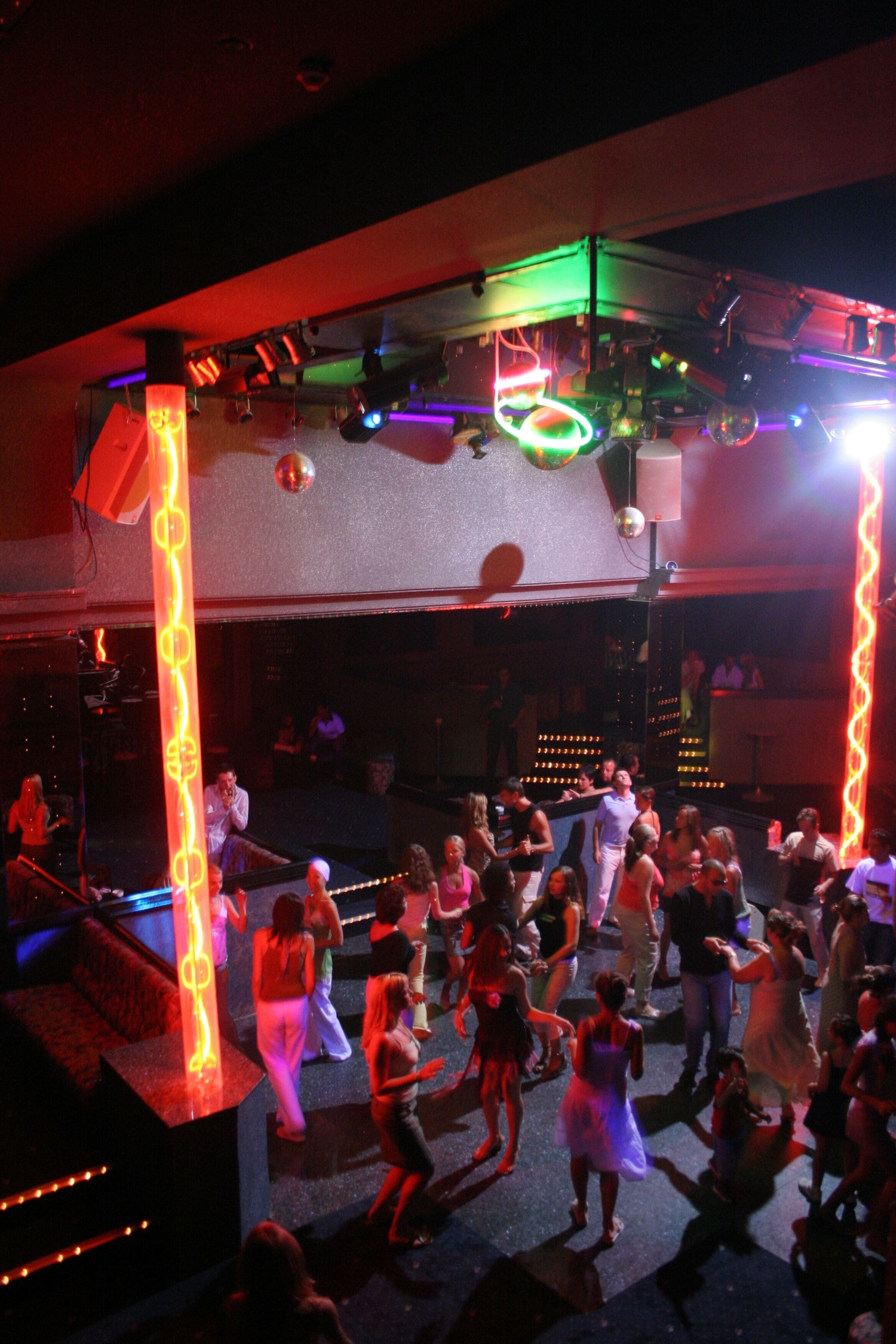 A crowded dance floor with people dancing, illuminated by colorful stage lights.