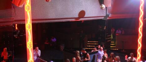 A crowded dance floor with people dancing, illuminated by colorful stage lights.