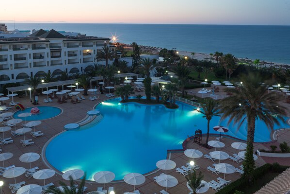 A resort with a large swimming pool, sun loungers, umbrellas, and a view of the ocean.
