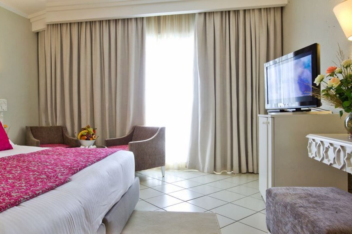Una habitación de hotel con una cama grande, dos sillas, un televisor y un escritorio con un florero.