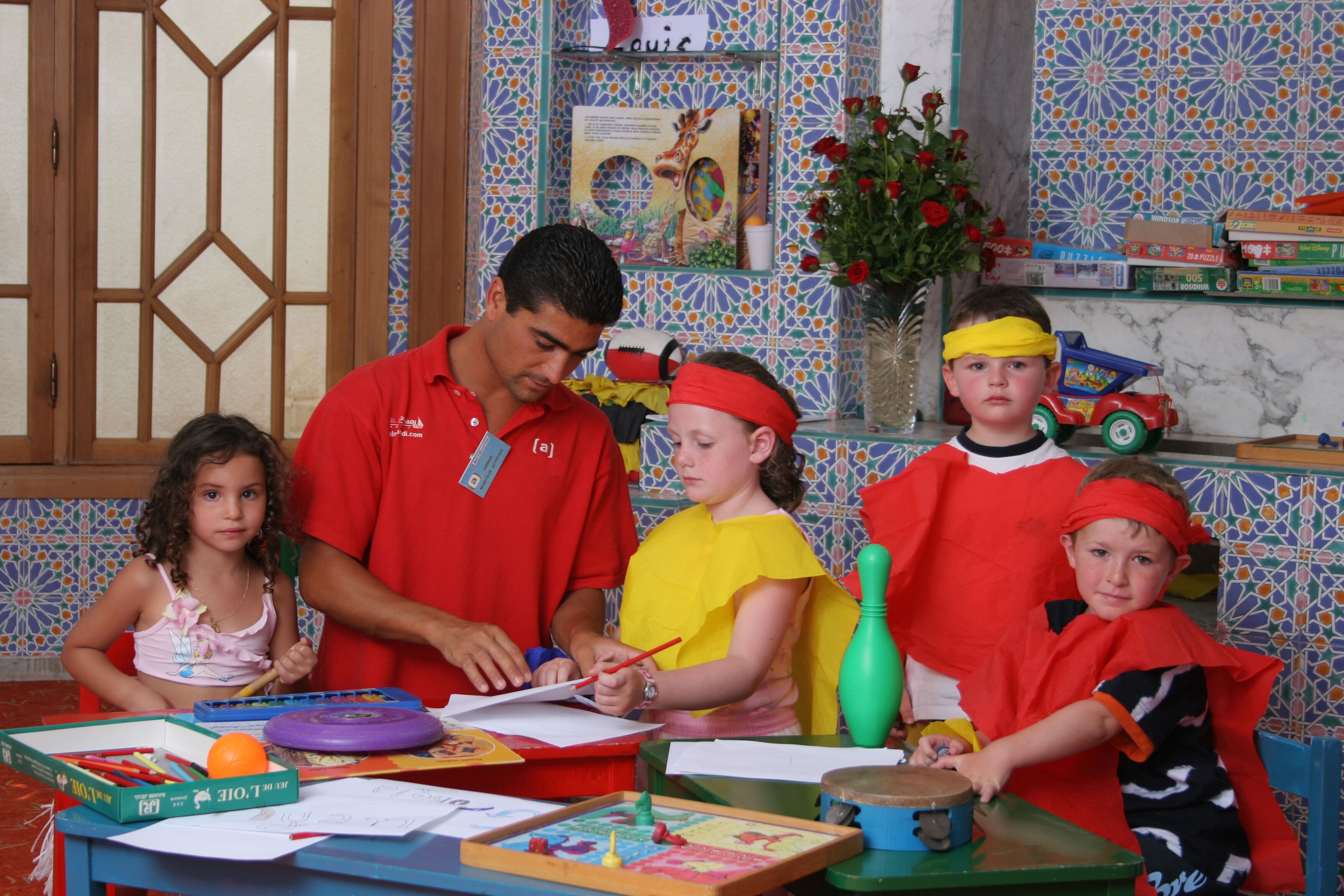 A classroom with children engaged in activities, a teacher assisting, and educational materials on the table.
