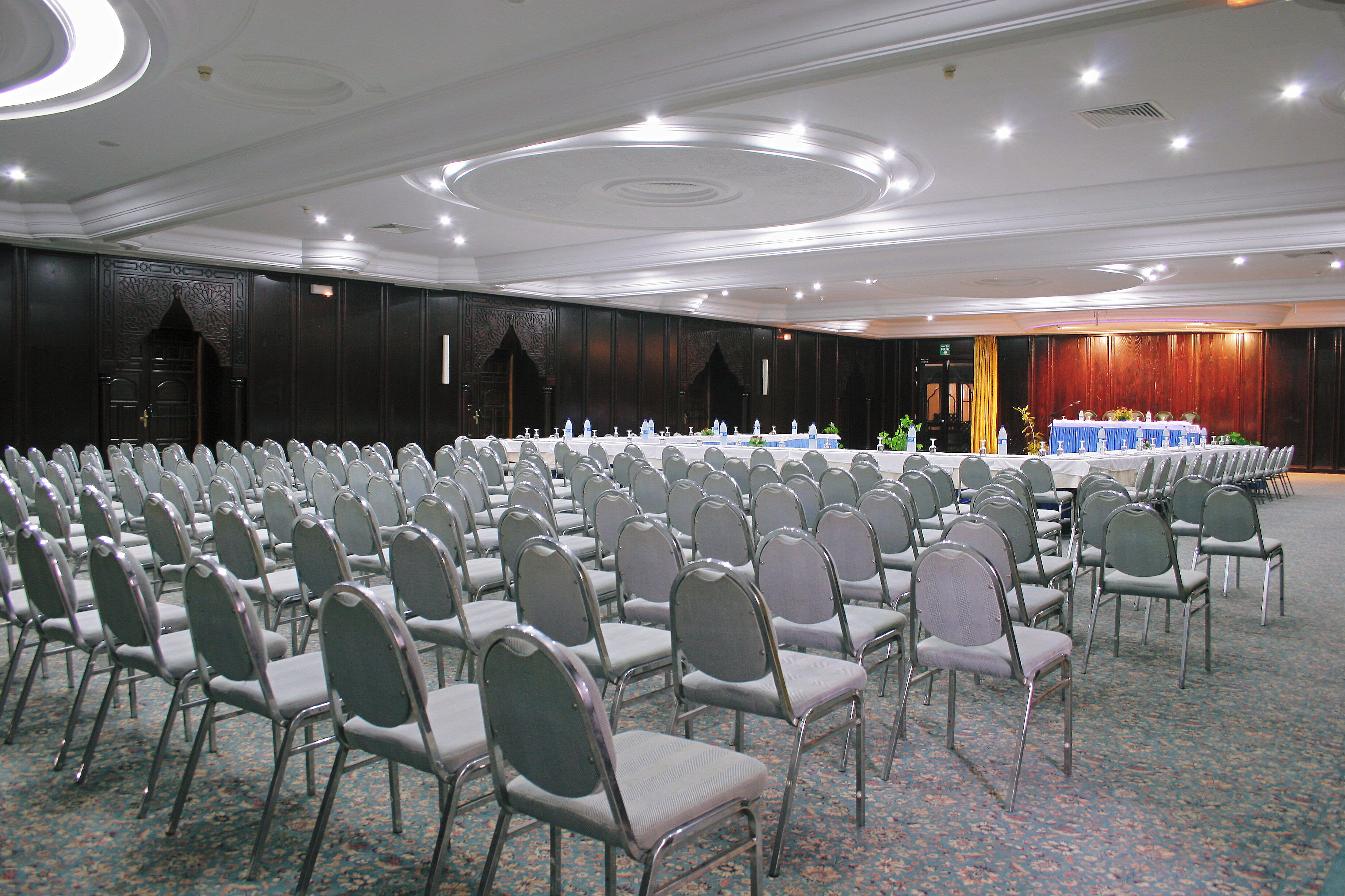 A conference room with rows of chairs, a long table, and a stage.