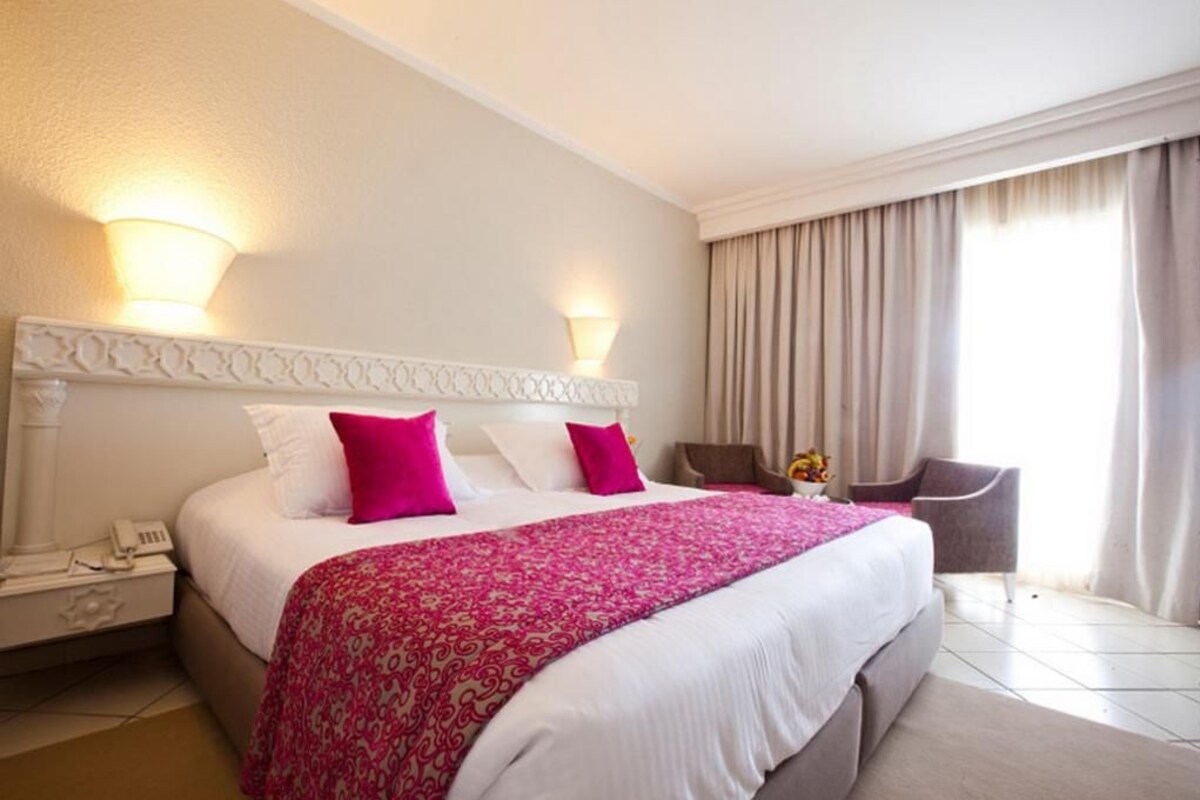 Habitación de hotel con una cama grande, dos lámparas de noche, una silla y una mesita de noche con teléfono.