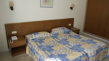 A bedroom with a wooden headboard, a bed with a patterned bedspread, bedside tables with lamps, and a wardrobe.