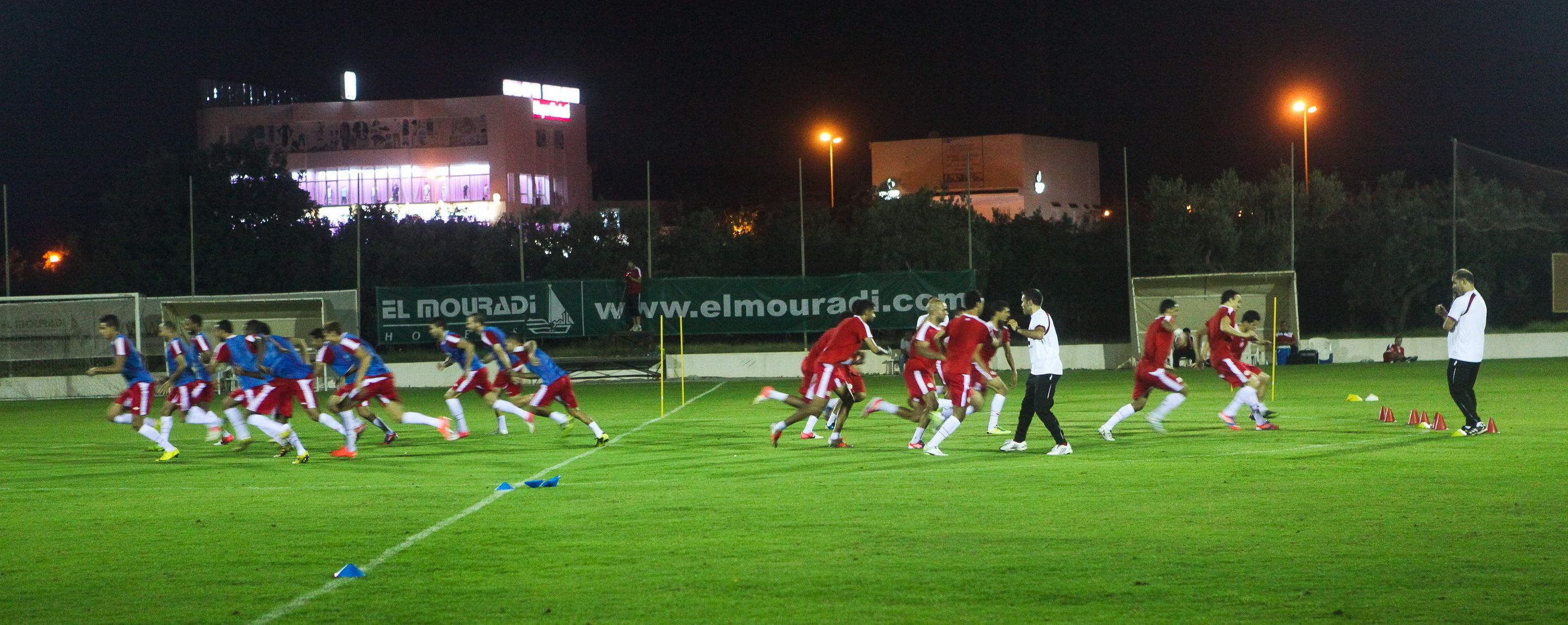 A nighttime soccer field with players in red and blue uniforms.