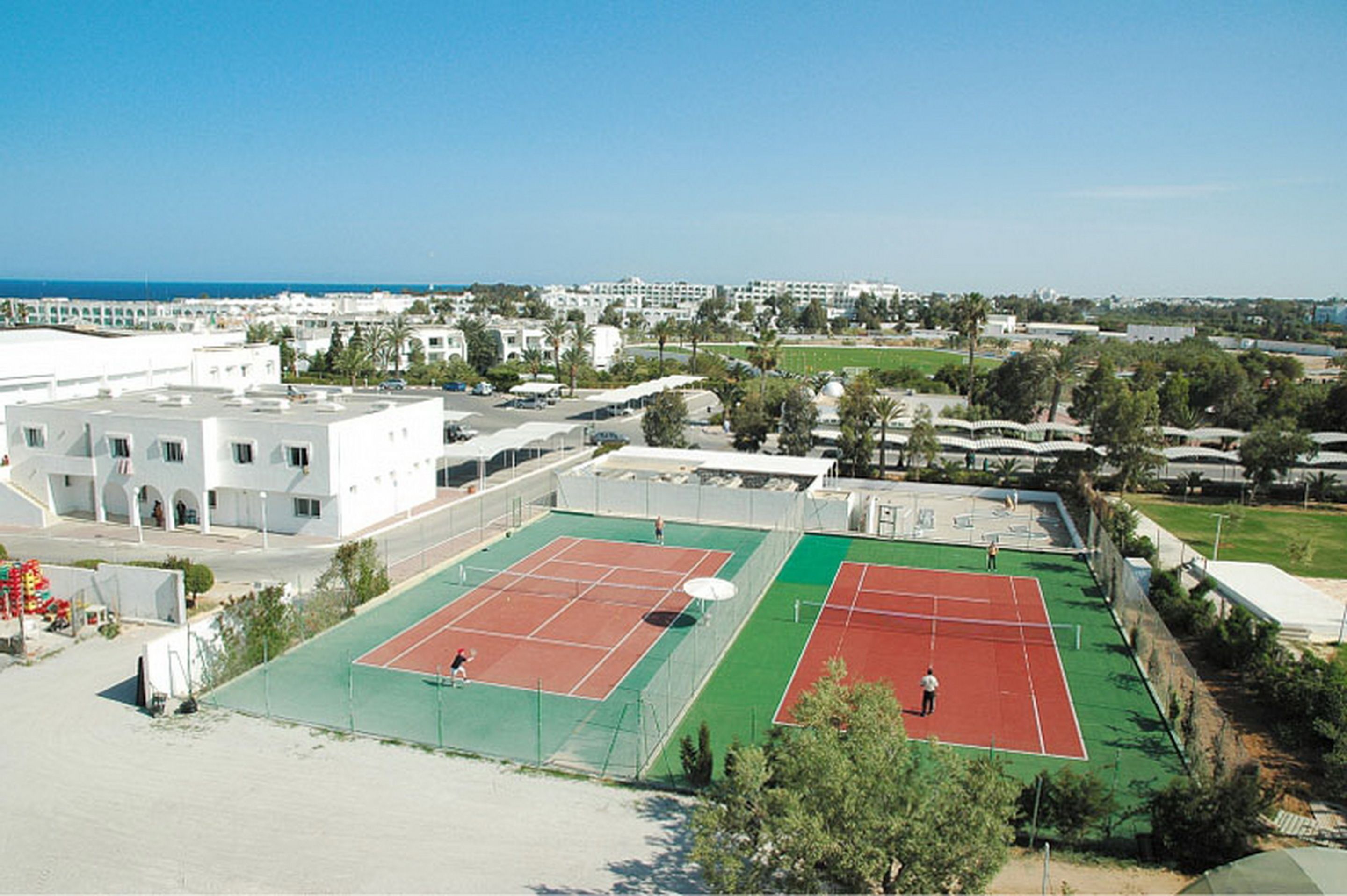 Ein Tennisplatz mit Netz, umgeben von Gebäuden und Grünflächen.