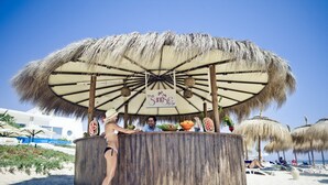 A beach bar with a thatched umbrella, wooden bar counter, and a sign reading "The Sunrise Bar". - El Mouradi Club El Kantaoui (Port El Kantaoui)