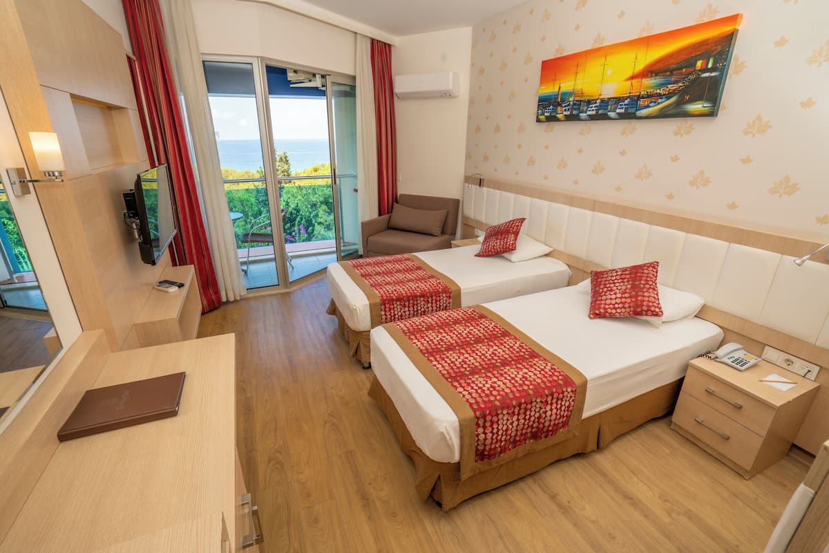 A hotel room with two beds, a desk, a chair, a nightstand, and a view of the sea.