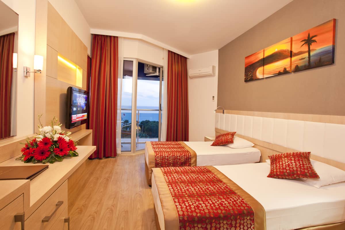 A hotel room with two beds, a TV, a painting, and a view of the sea.