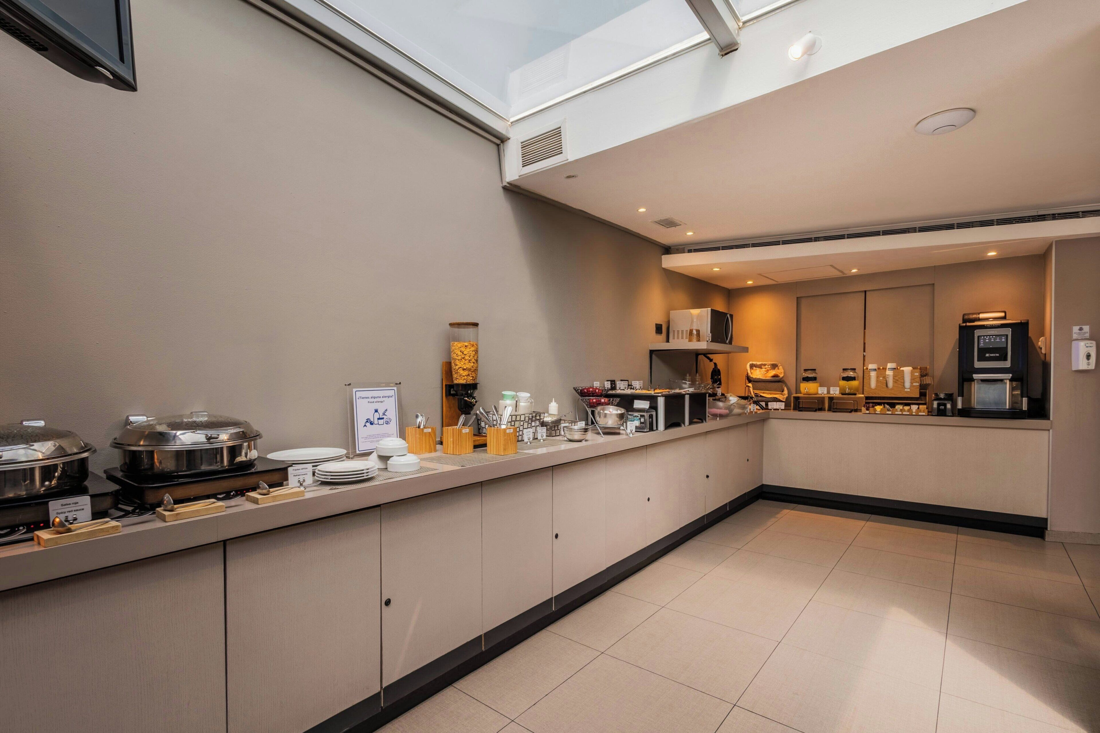 Une cuisine d’hôtel moderne, dotée d’un long comptoir, de différents postes de préparation et offrant une vue sur le ciel grâce à une verrière.