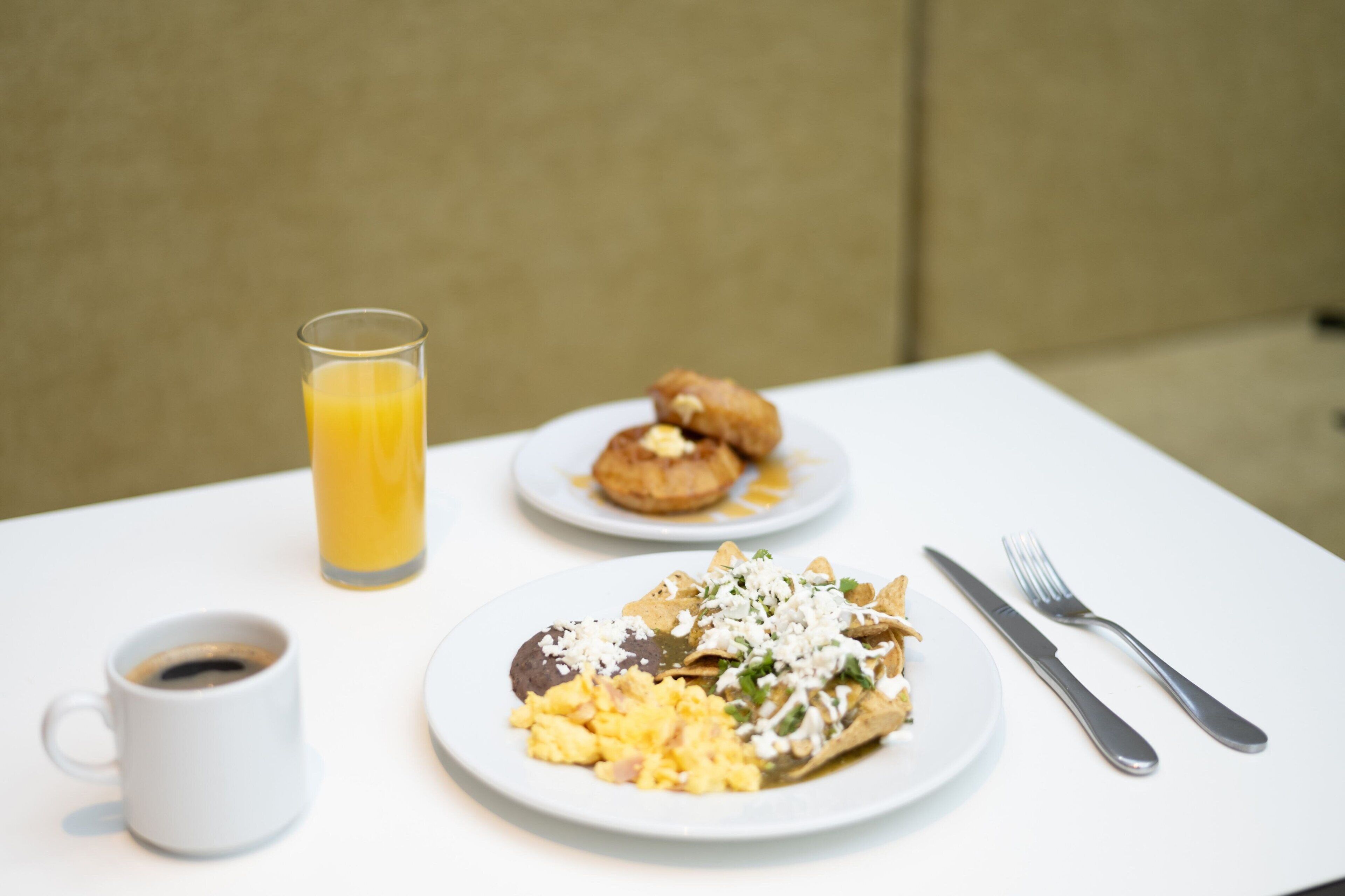 A breakfast setting with a plate of chilaquiles, a glass of orange juice, and a cup of coffee on a white table.